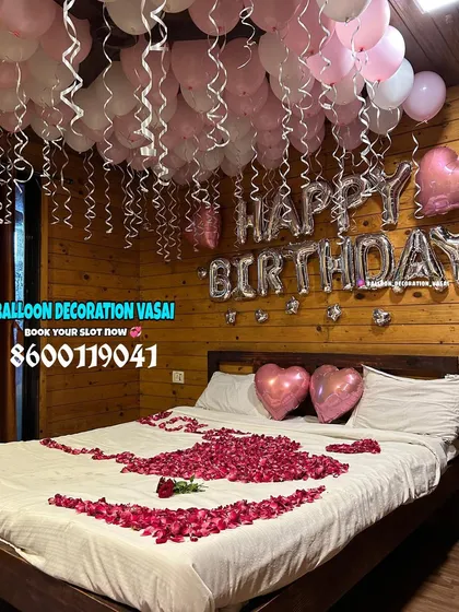 A closer look at the rose petal art on the bed, with two heart-shaped balloons. The silver "Happy Birthday" balloons stand out against the warm wooden walls of the farmhouse room.