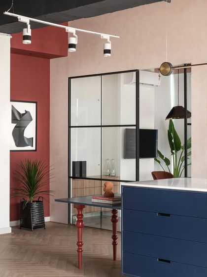 To break up a plain corner near our material island, I added a bold red accent wall that flows with the studio's theme. A beautiful piece of abstract art and a statement plant complete this little nook, giving it character and energy.