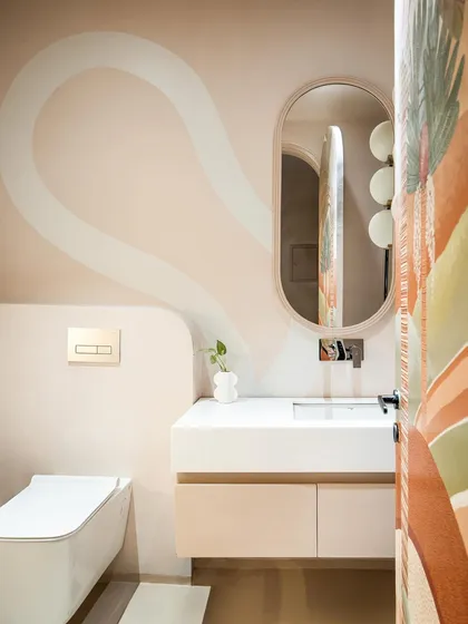 Inside the powder room, a serene canvas of soft beige tones is animated by an off-white ribbon-like shape that glides along the walls. Rounded corners and a floating vanity create a feeling of minimal, spacious beauty.