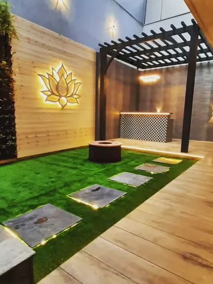 A full view of the backyard lounge, with the pergola-covered bar area, a central fire pit, and a backlit lotus wall feature.