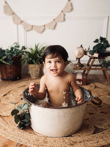 The joy of a splash session is evident in this baby's excited expression and playful splashing. The rustic, botanical background adds a natural touch.