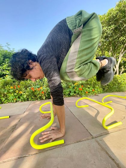 Using mini-hurdles as props, a practitioner holds a crow pose. This creative approach to yoga builds arm balance strength and adds a playful element to the practice.