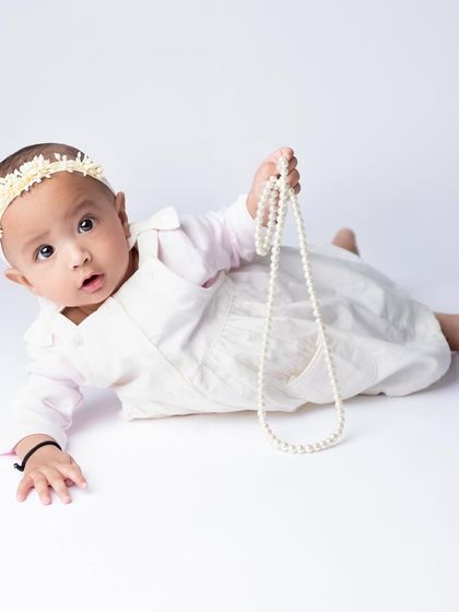 This little one is striking a pose with her pearls. The clean white background ensures that nothing distracts from her sweet face and playful gesture.