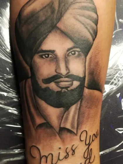 A memorial portrait tattoo of a man in a turban, with the script "Miss You Dad" below. The shading on the beard and eyes brings the portrait to life.