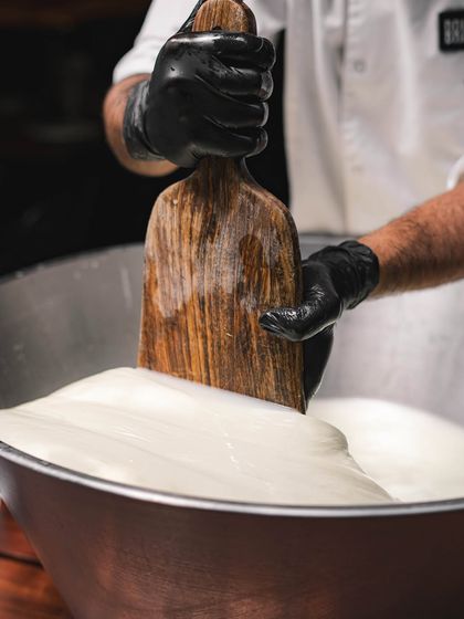 A large batch of mozzarella being stretched with a wooden paddle. We make our cheese in-house every day to ensure it's always fresh.