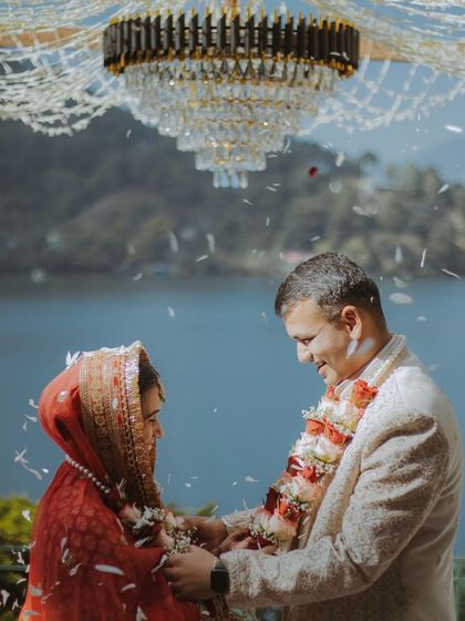 A magical moment during the Jaimala exchange, with petals falling as the couple stands beneath a grand chandelier by the lake.