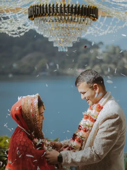 The jaimala exchange at a stunning lakeside wedding, with a crystal chandelier hanging over the mandap.