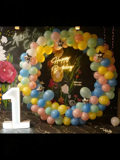 A first birthday party setup at a cafe, featuring a pastel balloon ring and a light-up number '1'.
