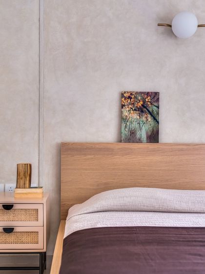 Surrounded by lush greenery, this master bedroom is a minimal, autumnal paradise. The simple wooden bed frame and cane nightstand are set against a textured wall, creating a sense of calm and connection to nature.
