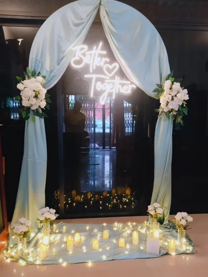 For this intimate home engagement, I created a romantic entryway using a soft pastel arch, white floral arrangements, and a custom 'Better Together' neon sign. The warm fairy lights and floor candles add a magical glow, perfect for evening celebrations.