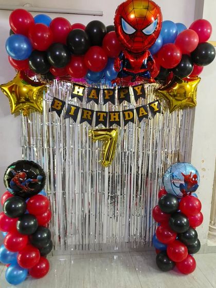 A simple and effective Spiderman theme for a 7th birthday. This home setup includes a shimmer curtain, balloon pillars with Spiderman foils, and a 'Happy Birthday' banner.