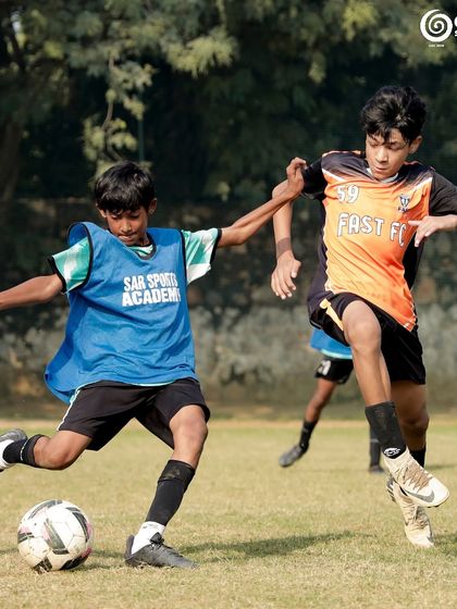 A GSC player in a blue bib dribbles past a Fast FC opponent.