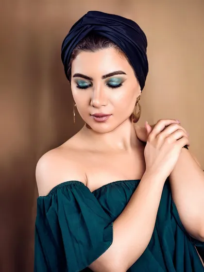 A beauty shot featuring vibrant turquoise eyeshadow, complemented by a black turban and gold earrings. The composition and color palette create a chic and classy portrait.
