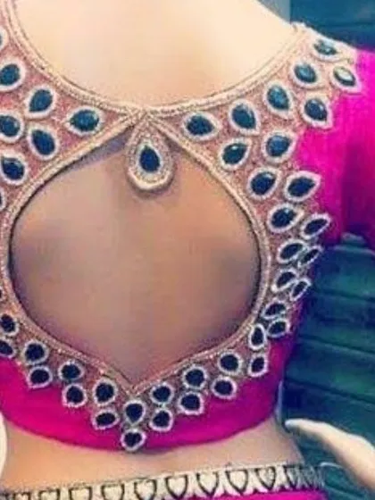 A bright pink blouse with a teardrop-shaped open back, outlined with heavy stone work. We specialize in creating statement blouses for weddings and parties.