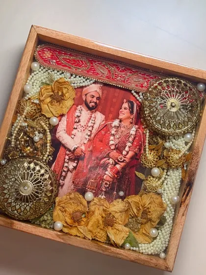 A close-up of a varmala preservation frame featuring a beautiful wedding photo. The intricate details of the garland, including the golden ornaments, are perfectly captured in glossy resin.
