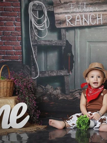 A happy little cowboy sitting on the ranch floor. The reflection on the floor adds a professional touch to this rustic, fun-filled first birthday photoshoot.