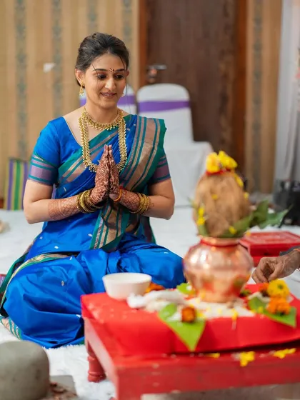 The bride participating in her engagement puja, looking serene and elegant with a simple updo and natural makeup.