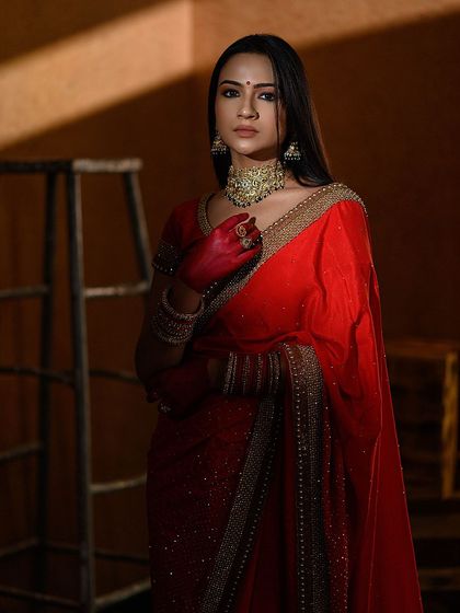 A dark and moody portrait in a red saree. The dramatic lighting from the side creates interesting shadows and highlights the model's features.