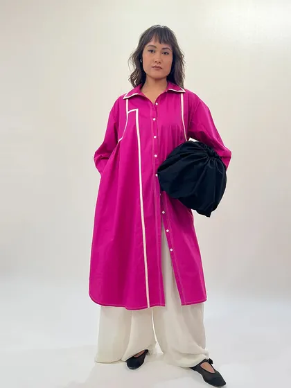 Draped in confidence, colored in power. This model wears a fuchsia shirt dress over wide-leg pants, accessorized with a black potli bag for a modern ethnic look.