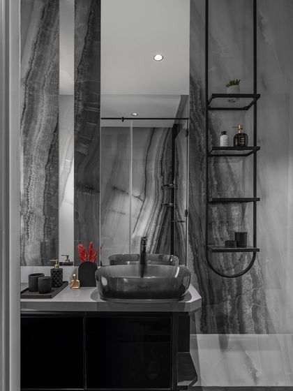 This bathroom features dramatic textured black and grey marble, adding depth and character. A sleek black vessel sink and a minimalist hanging storage unit ensure the space is both functional and beautiful.