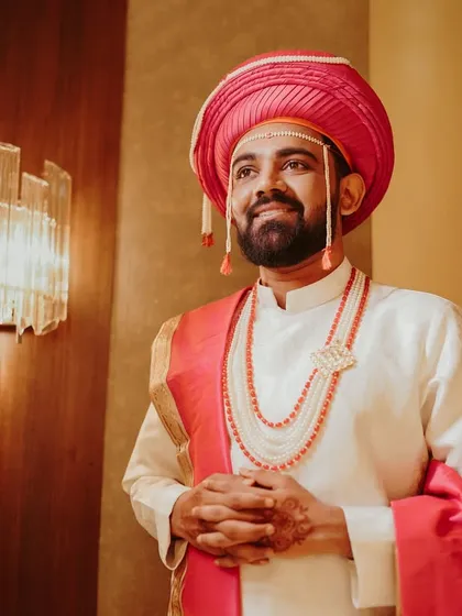 A portrait of a handsome Marathi groom in his traditional wedding attire, including the pink 'pheta' and pearl necklaces. He looks ready and excited for his wedding ceremony.