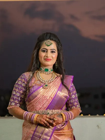 For my sister Sushma's reception, we went for a glamorous and sophisticated look. I created a soft glam eye with a hint of shimmer and a bold lip, paired with a modern half-up hairstyle with loose waves. This style perfectly complemented her elegant purple and gold saree and the evening's celebratory atmosphere.