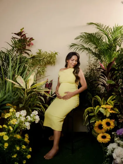 A serene solo portrait of the mother-to-be in our indoor garden. Seated amongst the plants and flowers, she looks down at her bump in a moment of quiet connection.