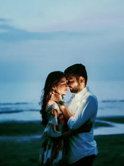 An intimate embrace with fairy lights draped around the couple, set against the twilight sky of a beach. This creative use of lighting adds a magical and romantic glow to the portrait.