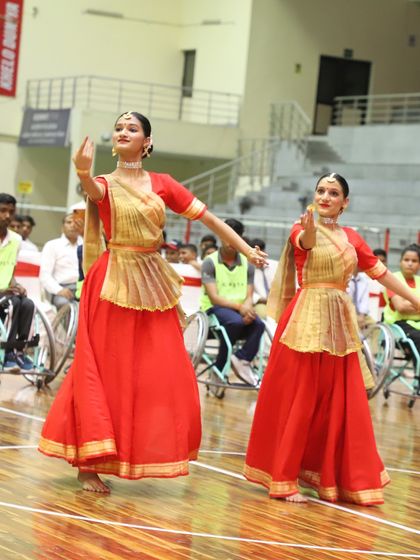 Dancers in traditional attire perform for an audience that includes athletes in wheelchairs. Our National Sports Day celebrations are a blend of sport and culture, promoting unity.