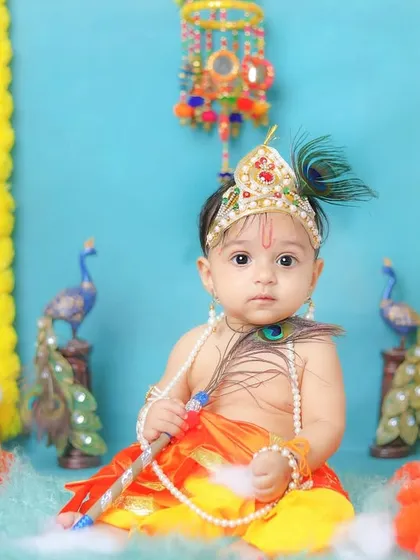 A curious little Kanha, holding his peacock feather and looking directly at the camera. A perfect, engaging portrait.