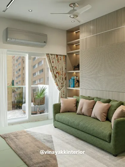 This living space combines a comfortable green sofa with a textured, fluted wall panel for a touch of modern sophistication. Large windows and sheer curtains allow for plenty of natural light, creating a serene and airy corner perfect for relaxation.
