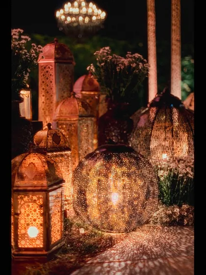 A collection of beautifully detailed Moroccan lanterns. The light filtering through the intricate patterns creates a warm, mesmerizing effect, essential for the Arabian Nights atmosphere.