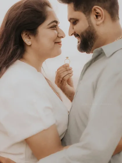 A close-up of a couple about to share a kiss, with the engagement ring held between them. A creative and romantic shot from a beach pre-wedding session.
