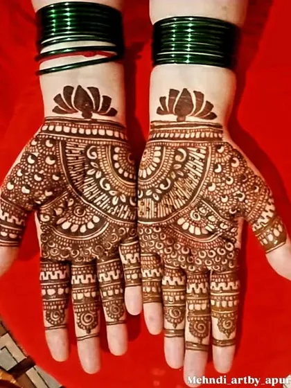 This is a classic palm-focused design with a lotus motif at the wrist and a detailed mandala pattern. The green bangles complement the henna beautifully, showing how it will look as part of a full outfit.