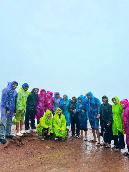 A group of travelers in colorful raincoats standing on a hilltop, completely enveloped in the monsoon mist.