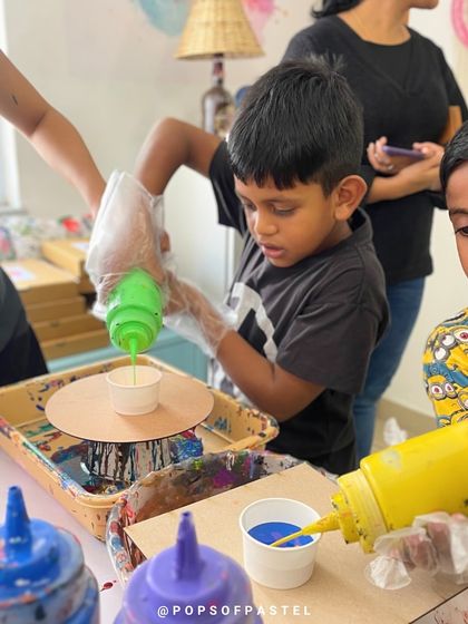 Two young boys watch intently as they mix and pour colors, completely captivated by the fluid art process at a birthday workshop.