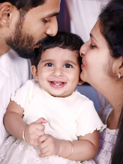 A happy family portrait with a smiling baby girl getting kisses from both mom and dad.