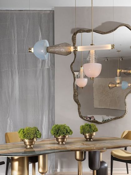 A single Luna Kaleido pendant with soft pink and blue glass is elegantly reflected in a large mirror, doubling its visual impact. This shows a creative way to integrate the light into a dining space.
