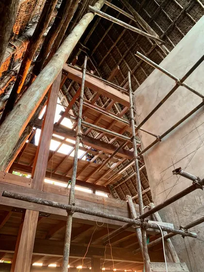 Looking up into the timber and thatch roof of the spa. The scaffolding shows the scale of the structure, which is designed to be both grand and intimate, with natural light filtering through the wooden beams.