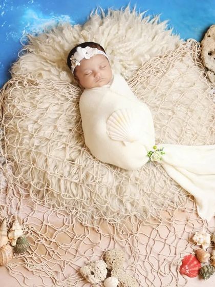 A beautiful mermaid-inspired beach theme. The baby is swaddled to look like a mermaid, resting on a fishing net with seashells for a magical ocean portrait.