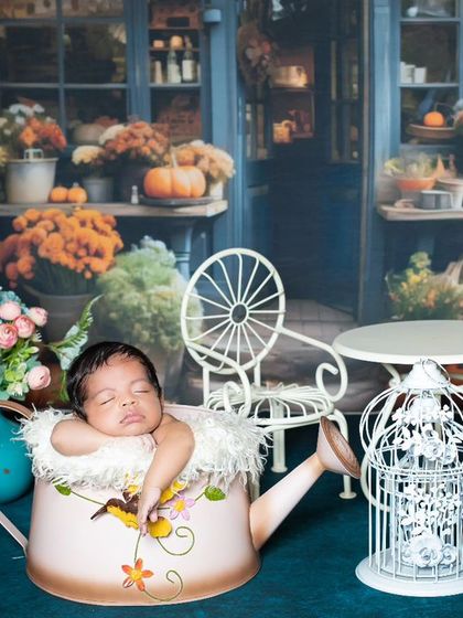 A newborn sleeping in a watering can, surrounded by a beautiful flower market scene.