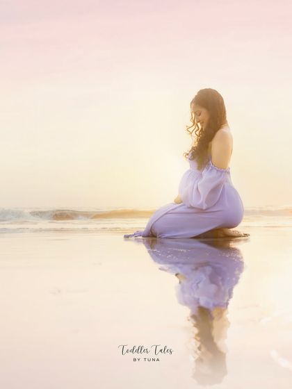 A moment of peace by the ocean. The reflection in the water, the soft golden light, and the gentle waves create a serene and beautiful setting for this maternity portrait.