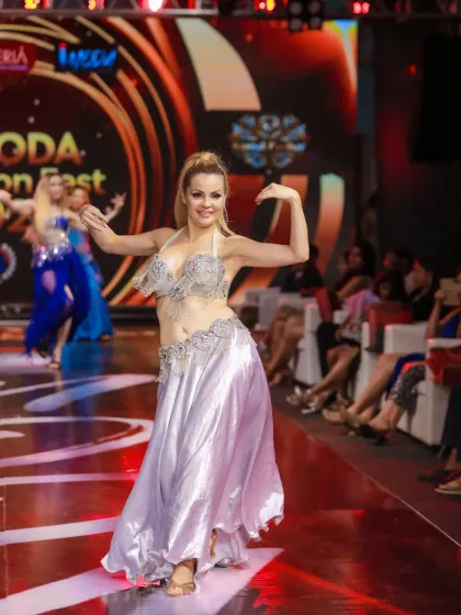 A performer in a shimmering silver outfit during her belly dance routine. The photo captures the flow of the fabric and the joy in her performance.