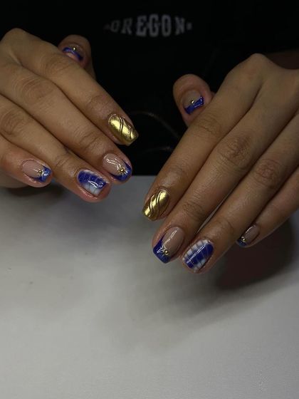 A bold and artistic set on short, square nails, featuring a mix of blue, white, and gold chrome.