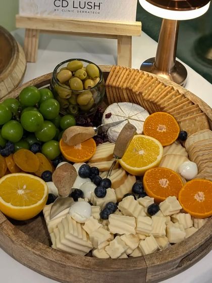 A bountiful cheese platter featuring a mix of hard and soft cheeses, olives, grapes, and fresh citrus. This board was part of a wellness-focused event for a dermatology clinic.