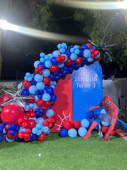 An action-packed Spiderman theme for a 3rd birthday, set up outdoors on a lawn. The decoration includes a large Spiderman cutout and a dynamic red and blue balloon arch.