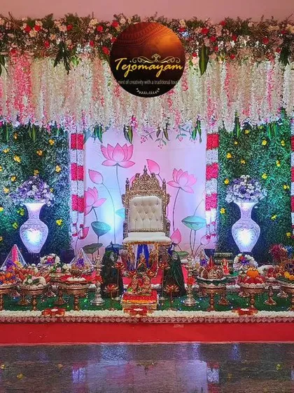 A baby shower setup with a lotus-themed floral backdrop and hanging garlands. The plate decoration is rich and colorful.