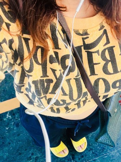 A top-down view of a casual and comfortable outfit. The graphic sweatshirt, dark joggers, and bright yellow slides create a fun and relaxed look for a simple day.