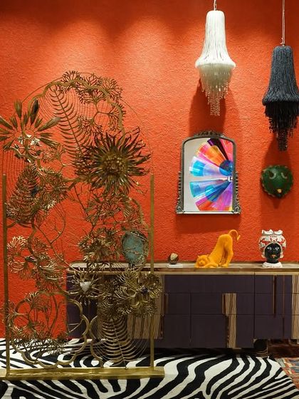 A visitor observes the curated eclecticism of the 'Bad Taste?' installation. The space combines a zebra-print rug, a gold-leafed screen, and a classic blue armchair to create a unified whole from seemingly disparate, audacious elements.