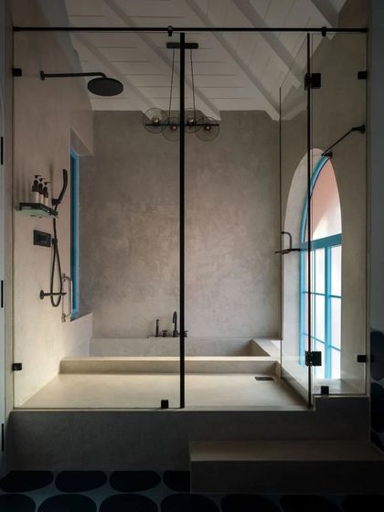 A view of the sunken tub in a bathroom at Baia Villas. The design uses a change in level to create a unique bathing experience, enclosed in glass but visually connected to the rest of the space. The micro-cement finish adds a raw, tactile quality.